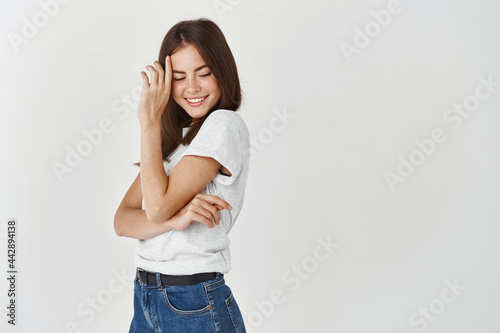 Beauty. Sensual brunette woman standing in profile, blushing and smiling, looking down coquettish, standing over white background © Cookie Studio