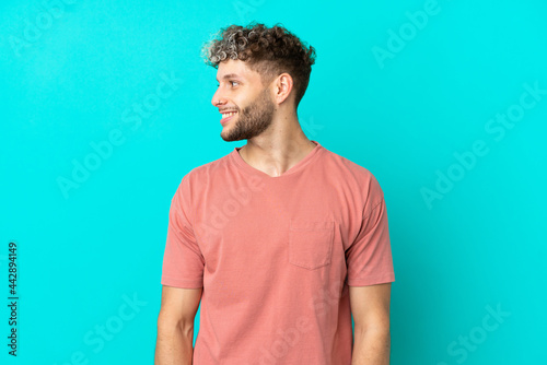 Young handsome caucasian man isolated on blue background looking side
