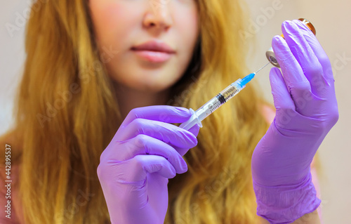 A young woman doctor wearing purple rubber gloves holds an injection syringe with a thin needle. Lip augmentation procedure, facial, body rejuvenation, mesotherapy. Aesthetic cosmetology. Beauty Salon