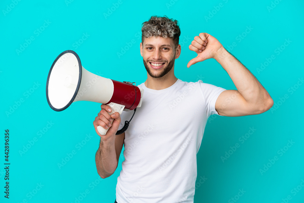 Young handsome caucasian man isolated on blue background holding a megaphone and proud and self-satisfied Young handsome caucasian man isolated on blue background holding a megaphone and proud and self-satisfied