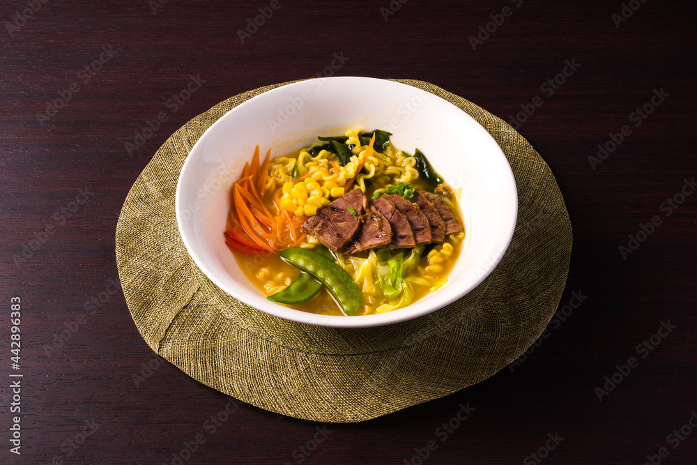 typical Asian dish, Ramen with vegetables, noodles and beef. Plate on dark background