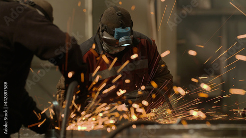 Metal workers in factory grinding with sparks
