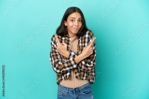 Young French woman isolated on blue background pointing to the laterals having doubts