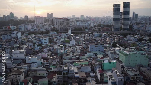 Different old small buildings surround large skyscrapers under bright sunlight and orange white sky at sunrise aerial view. Ho Chi Minh City, Vietnam.