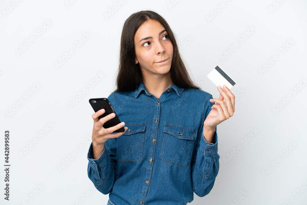 Young French girl isolated on white background buying with the mobile with a credit card while thinking Young French girl isolated on white background buying with the mobile with a credit card while thinking