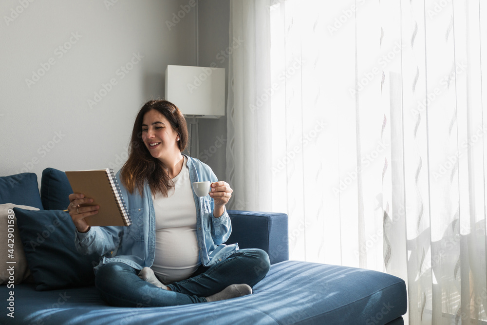 Cheerful pregnant woman drinking beverage on sofa at home Cheerful pregnant woman drinking beverage on sofa at home
