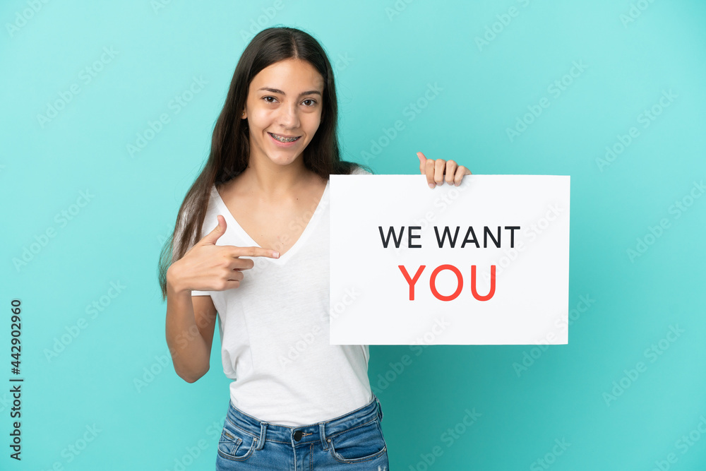 Young French woman isolated on blue background holding We Want You board and pointing it Young French woman isolated on blue background holding We Want You board and pointing it
