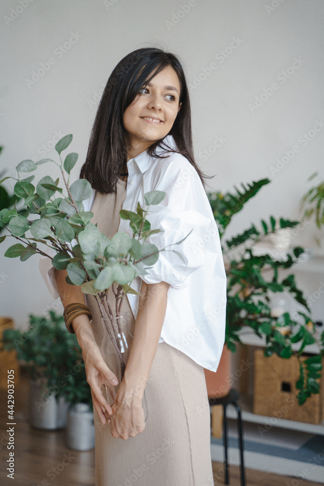 Young smiling woman holding a vase with eucalyptus branches at home. Naturalness and ecology concept Young smiling woman holding a vase with eucalyptus branches at home. Naturalness and ecology concept