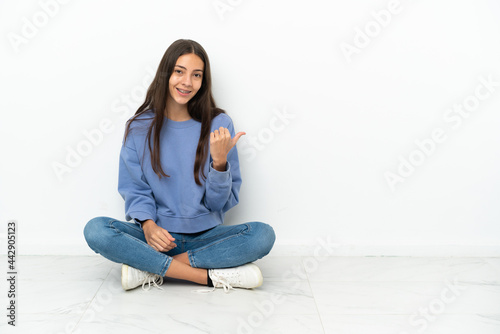 Young French girl sitting on the floor pointing to the side to present a product