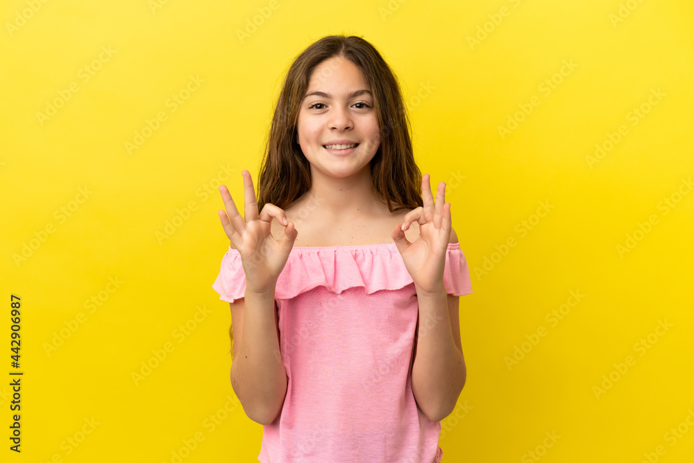 Little caucasian girl isolated on yellow background showing ok sign with two hands Little caucasian girl isolated on yellow background showing ok sign with two hands