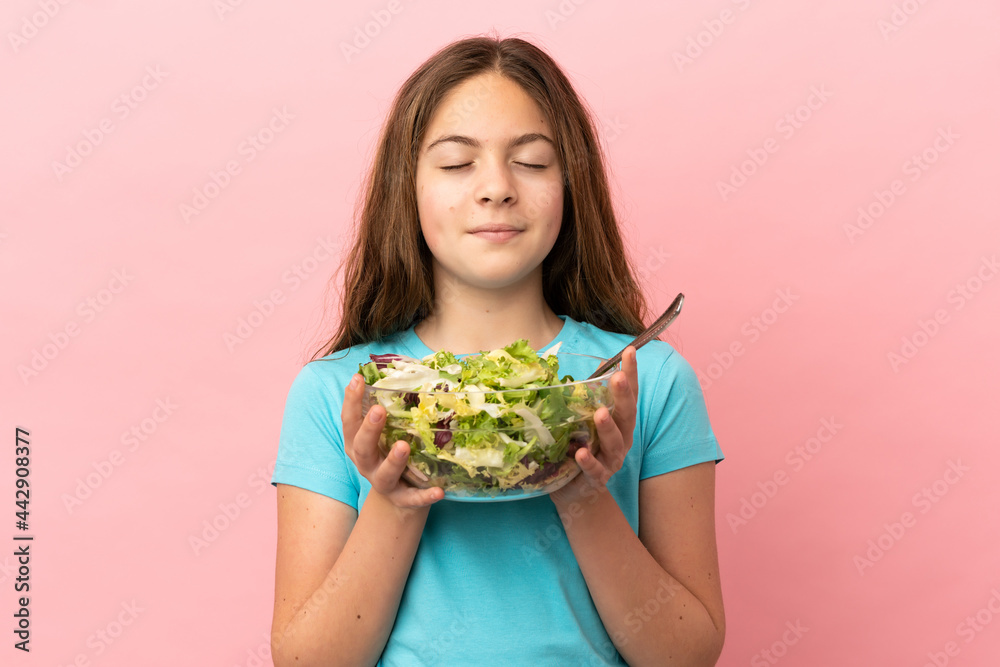 Little caucasian girl isolated on pink background holding a bowl of salad with happy expression