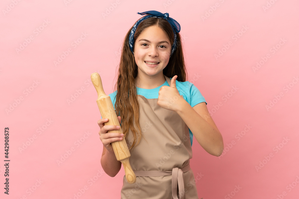 Little caucasian girl holding a rolling pin isolated on pink background giving a thumbs up gesture Little caucasian girl holding a rolling pin isolated on pink background giving a thumbs up gesture