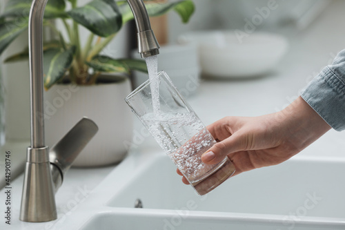Fotografie, Obraz Woman filling glass with water from tap in kitchen, closeup