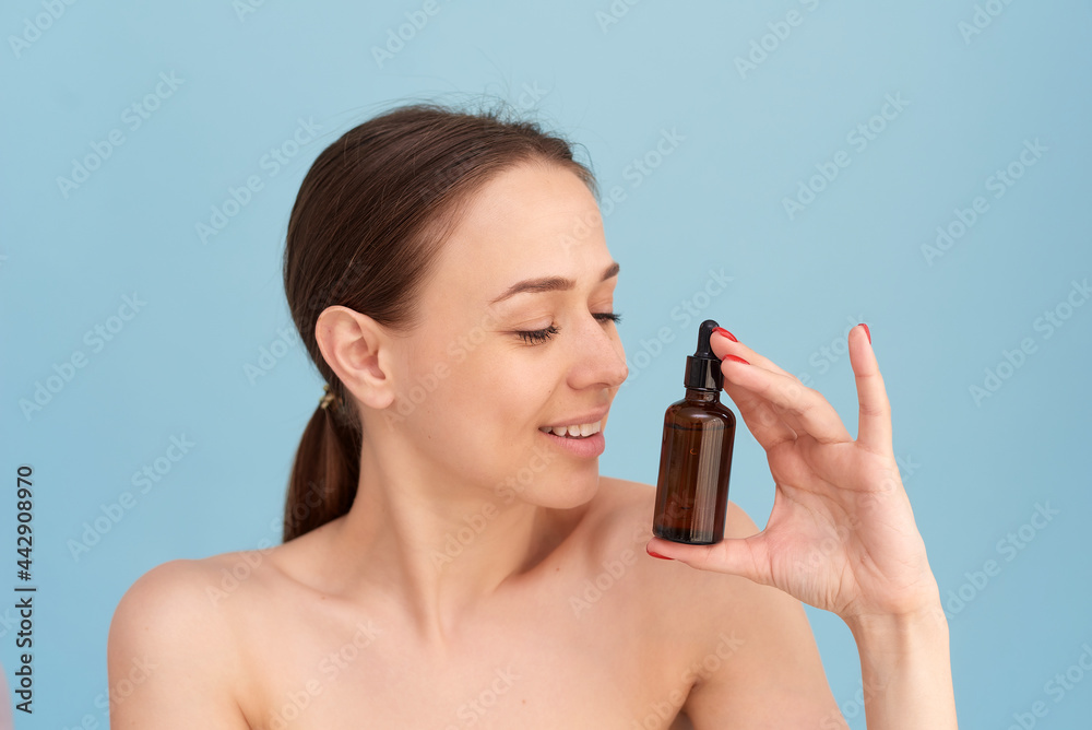 Smiling woman holding vitamin c serum near her face on blue background. Skin care and health concept Smiling woman holding vitamin c serum near her face on blue background. Skin care and health concept