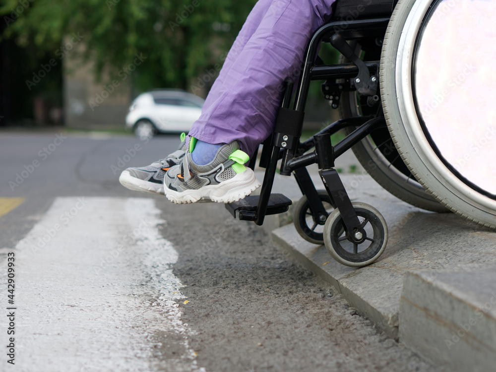 Obraz premium A paralyzed girl in a wheelchair prepares to run over the border in front of a pedestrian crossing. Risk of accident and crash. Uncomfortable environment. No face
