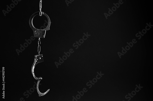 Classic chain handcuffs hanging on black background, space for text photo