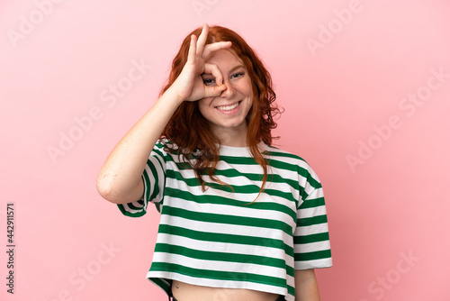 Teenager redhead girl over isolated pink background showing ok sign with fingers