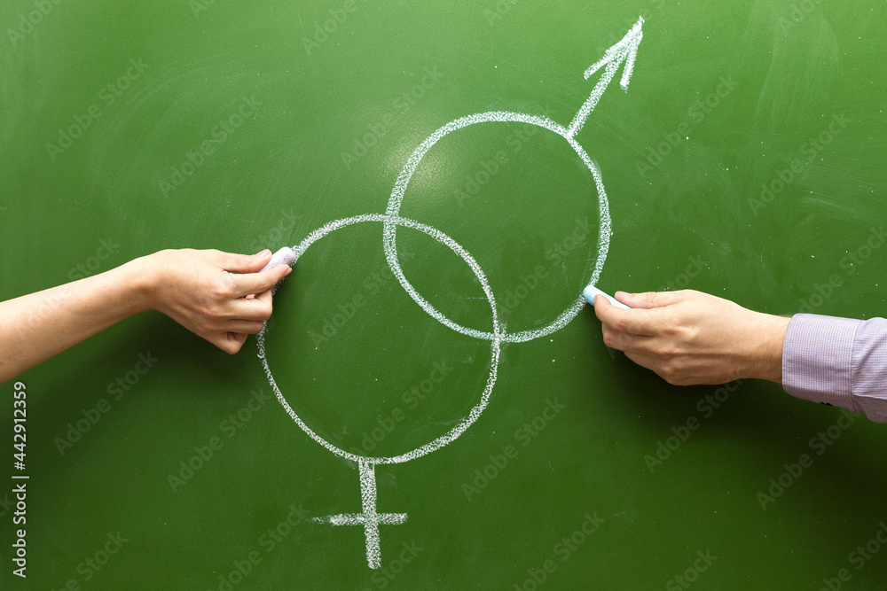 Male and female hands draw symbols of the masculine feminine principle with chalk on the blackboard. The concept of love at school..