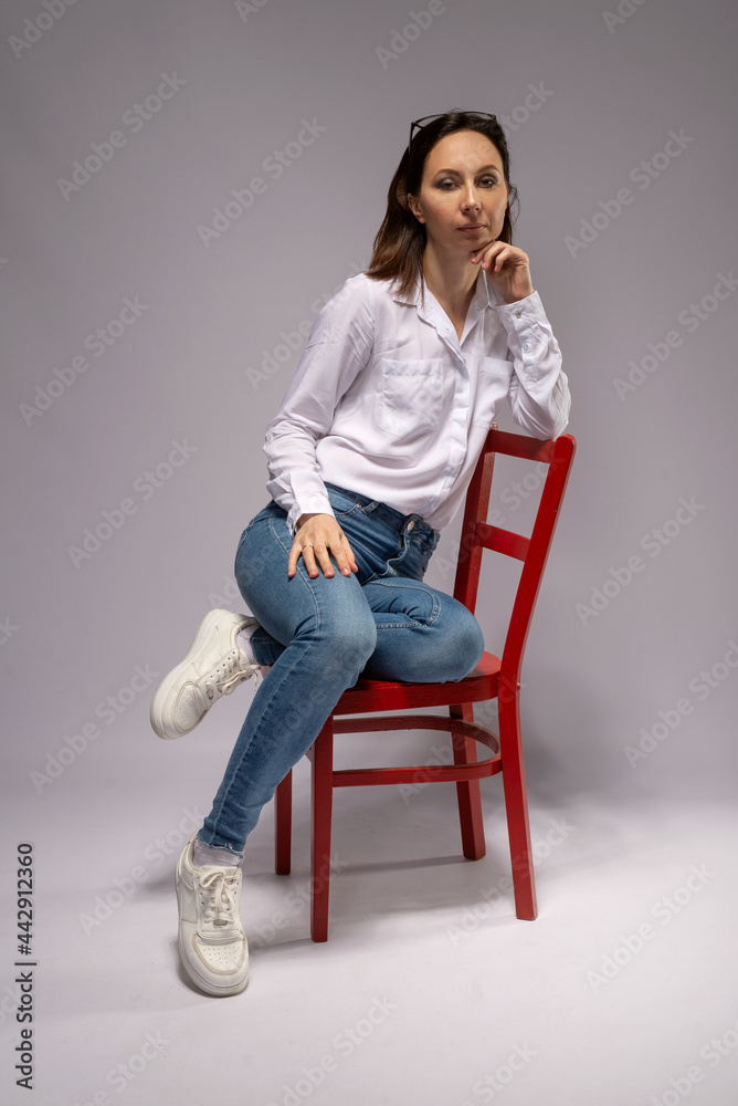 Young woman in a white shirt and jeans on a red chair. Young woman in a white shirt and jeans on a red chair.