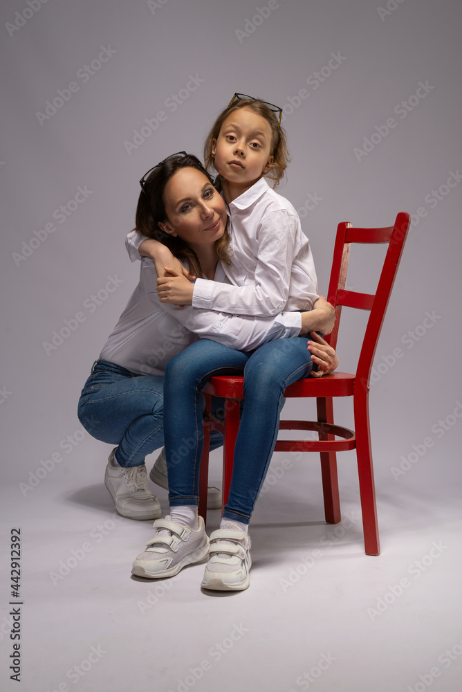Mom and daughter in jeans and white shirts on a gray background. Mom and daughter in jeans and white shirts on a gray background.