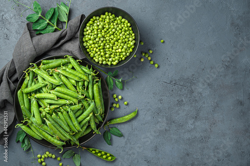 Pea pods and peeled peas on a dark gray background with space for copying. Top view, horizontal.
