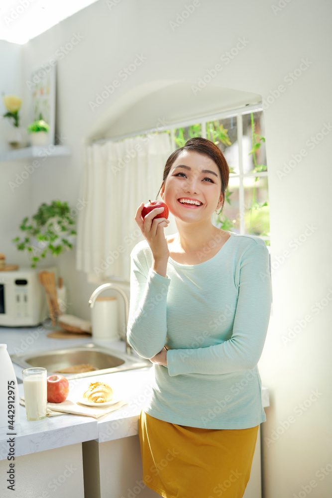 Beautiful girl holding red apple while standing in the home kitchen in the morning