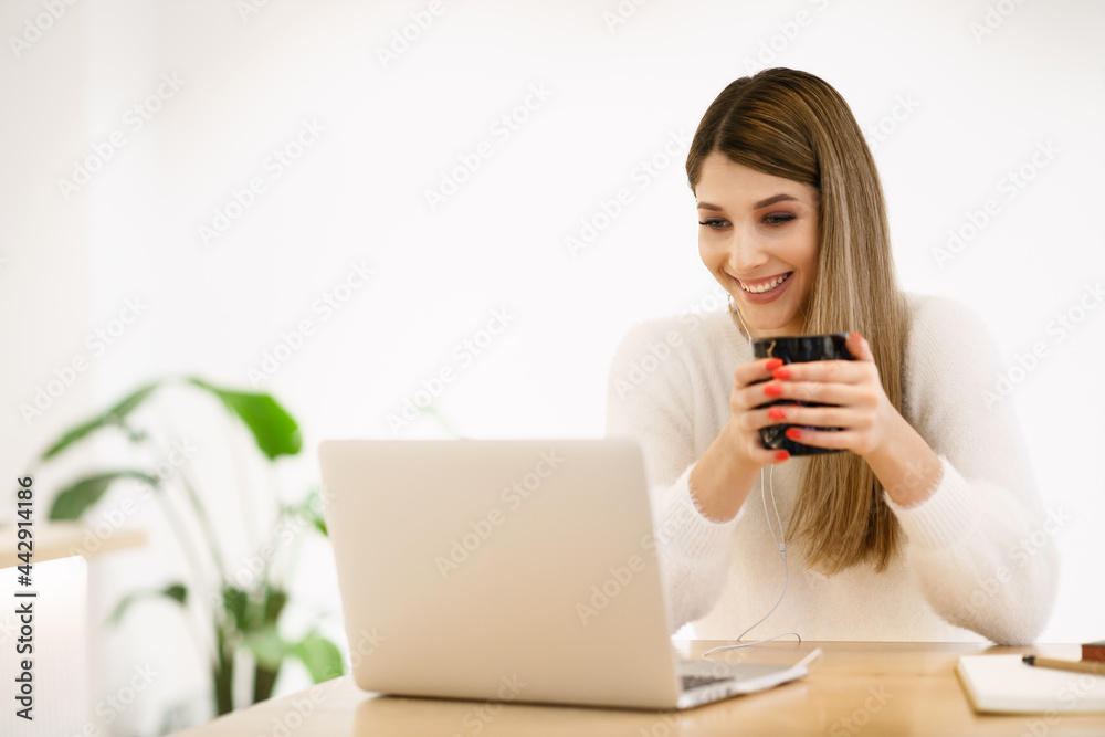 Beautiful young woman in casual clothing using laptop and smiling while working indoors Beautiful young woman in casual clothing using laptop and smiling while working indoors