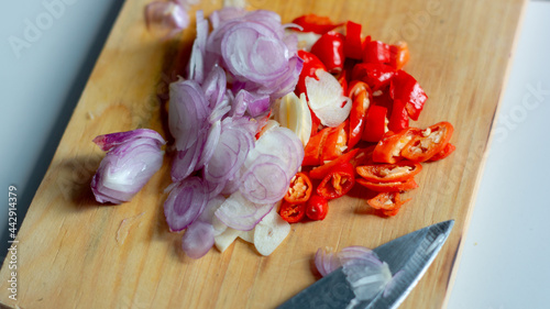 knife slices onion, garlic and chili on a cutting board