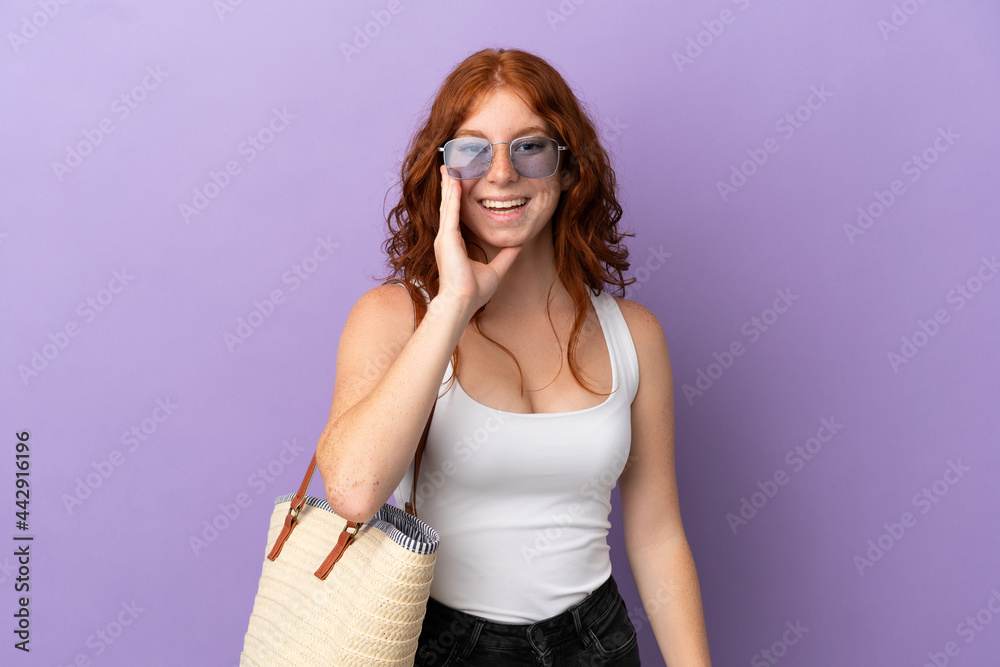 Teenager redhead girl holding a beach bag isolated on purple background shouting with mouth wide open Teenager redhead girl holding a beach bag isolated on purple background shouting with mouth wide open