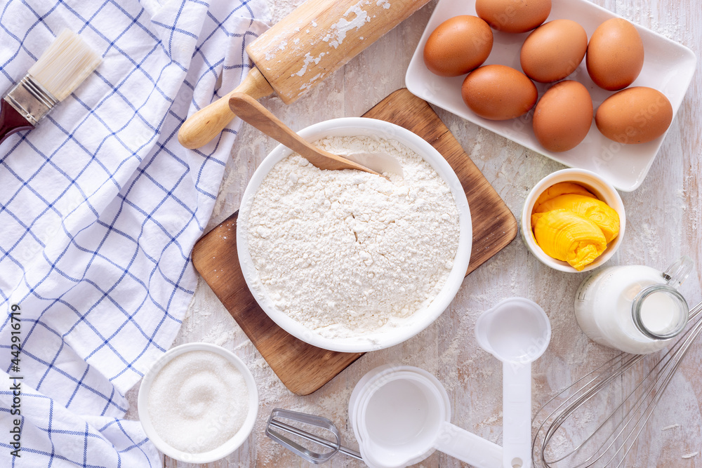 Homemade dough recipe (eggs, flour, milk, sugar) on a wooden table top view.