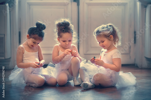 Three funny little ballerinas are eating chocolate candies in the ballet class. Image with selective focus, toning and noise effects.