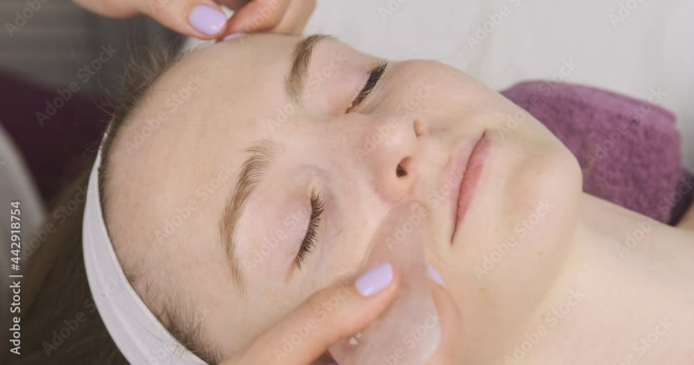 Young beautiful woman is massaged face by scrapering gua sha. Modeling procedure has been an oval face, a spa salon. Young beautiful woman is massaged face by scrapering gua sha. Modeling procedure has been an oval face, a spa salon.