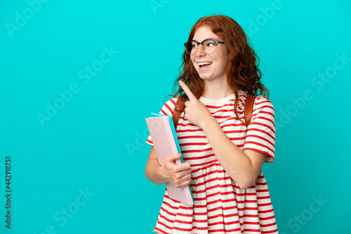 Student teenager redhead girl isolated on blue background intending to realizes the solution while lifting a finger up