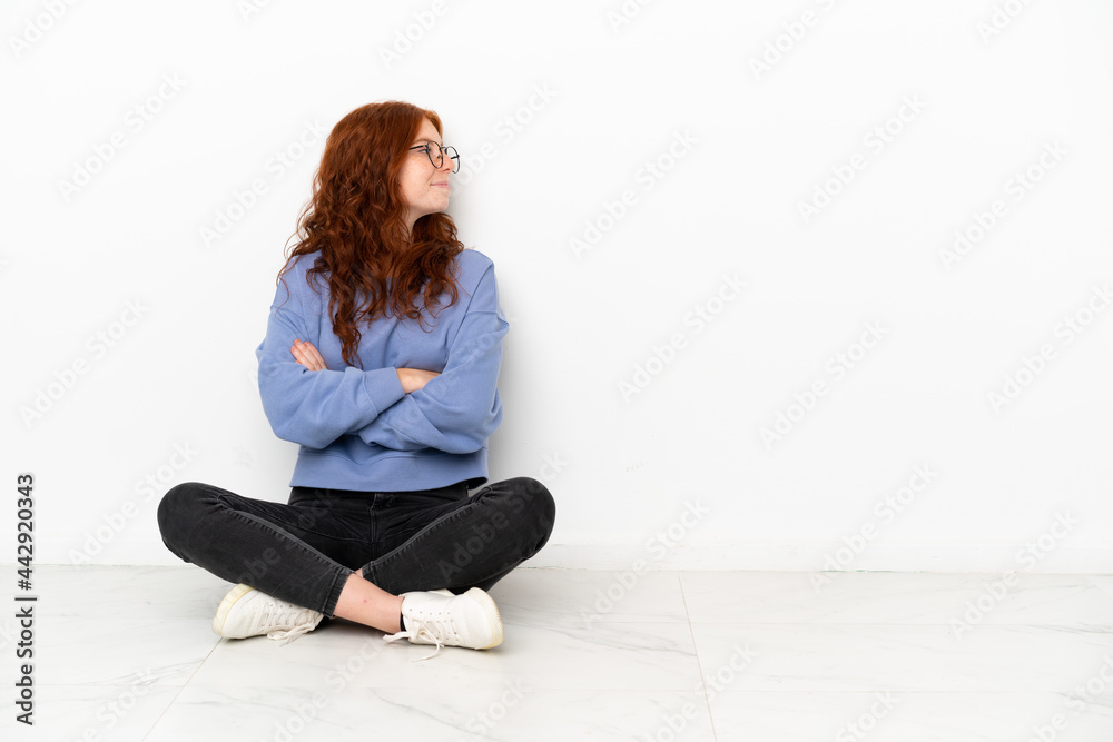 Teenager redhead girl sitting on the floor isolated on white background in lateral position Teenager redhead girl sitting on the floor isolated on white background in lateral position