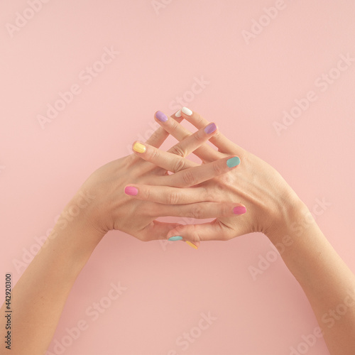 women hands with colorful nails on the pastel pink background. copy space.  summer modern tropical abstract art with female hand. minimal background idea with copy space