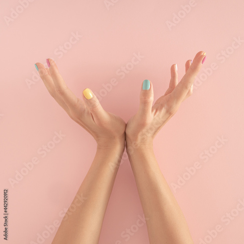 women hands with colorful nails on the pastel pink background. copy space. summer modern tropical abstract art with female hand. minimal background idea.