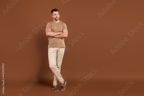 Photo of pretty confident young guy dressed beige clothes arms crossed looking empty space isolated brown color background