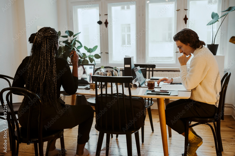 Affärskvinna i videosamtal sitter vid bord med man som arbetar på laptop hemma