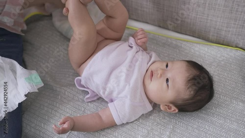close up view adorable newborn girl is babbling while her mommy is replacing the soiled nappy with a new one on the sofa in the living room.