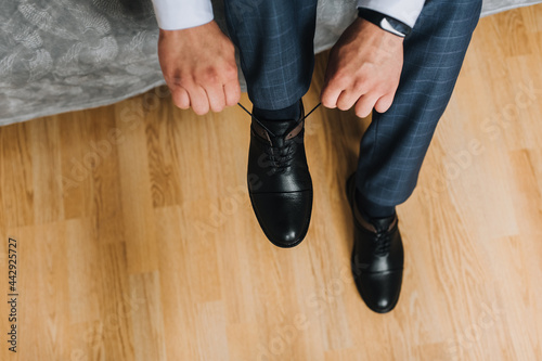 A man, a businessman, ties his shoelaces with his hands on shiny black leather shoes. Wedding portrait of the groom in the morning. Photography, concept, top view.