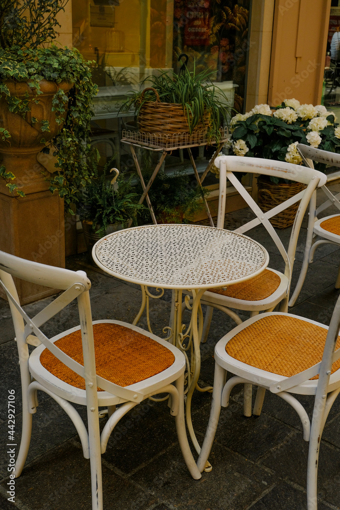 White wooden table with chairs across plants in pots in restaurant terrace. Cafe exterior. City life	
