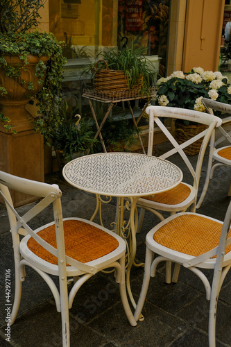 White wooden table with chairs across plants in pots in restaurant terrace. Cafe exterior. City life  