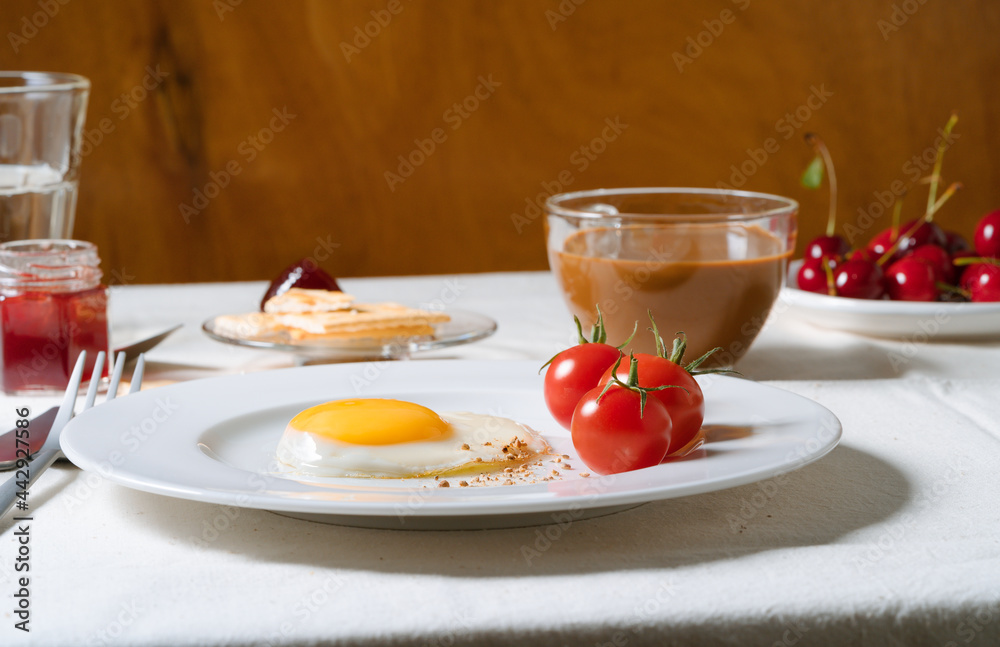 Fried egg with tomatoes on white plate, breakfast dining table Fried egg with tomatoes on white plate, breakfast dining table