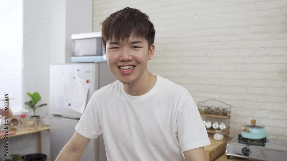 chinese male face close to the camera is waving hand with a big smile and sipping coffee while having a video chat in the kitchen at home. chinese male face close to the camera is waving hand with a big smile and sipping coffee while having a video chat in the kitchen at home.
