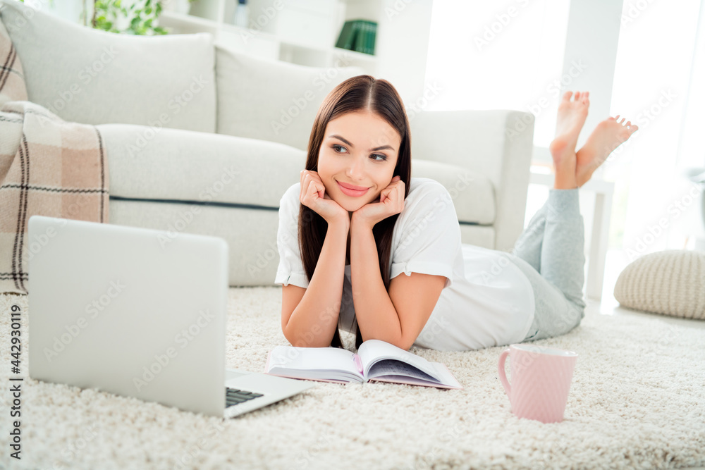 Fototapeta premium Photo of adorable lovely lady open notepad look screen laptop lay floor wear white t-shirt in room indoors
