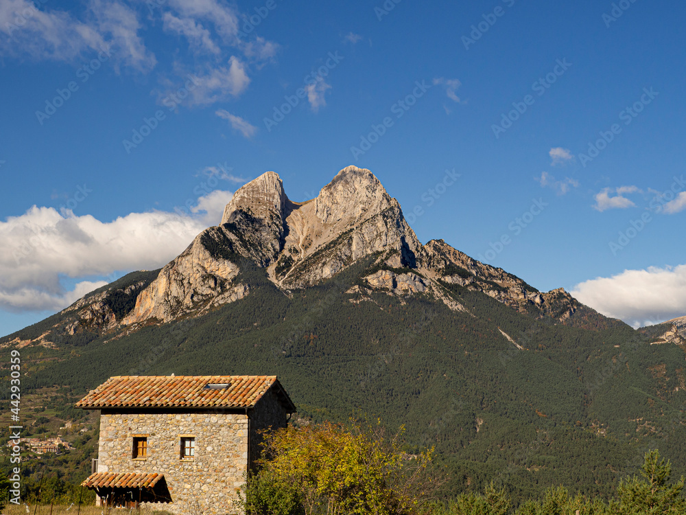 Montaña del Pedraforca en Cataluña, con una forma singular, sobre un cielo azul con nubes blancas sombreando el valle con árboles de colores de otoño, marrones y amarillos en Octubre de 2020.