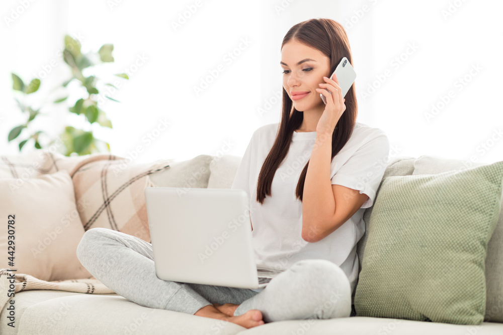 Photo of sociable lady hold laptop look screen have phone wear white t-shirt sit couch in room indoors Photo of sociable lady hold laptop look screen have phone wear white t-shirt sit couch in room indoors