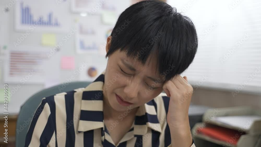 closeup asian female manager is rubbing her temple with finger and fist while suffering headache in the office. closeup asian female manager is rubbing her temple with finger and fist while suffering headache in the office.