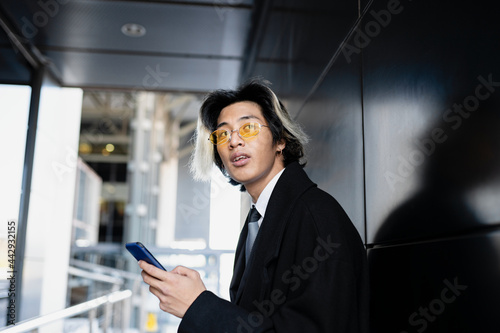 Ethnic businessman chatting on smartphone against building wall