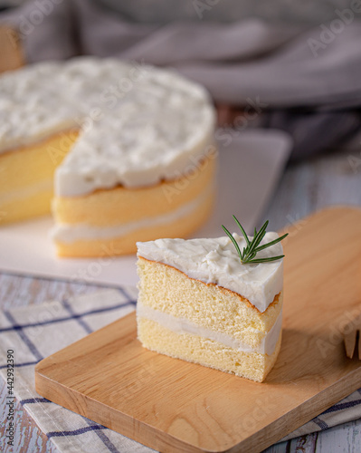 Coconut cake - slice of homemade coconut cake topping with rosemary on wooden board.